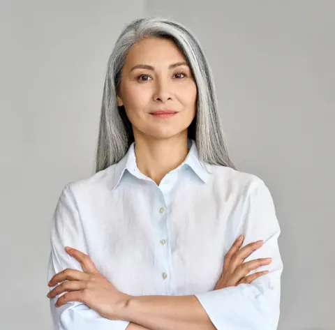 Smiling woman with long grey hair in a white shirt, arms folded