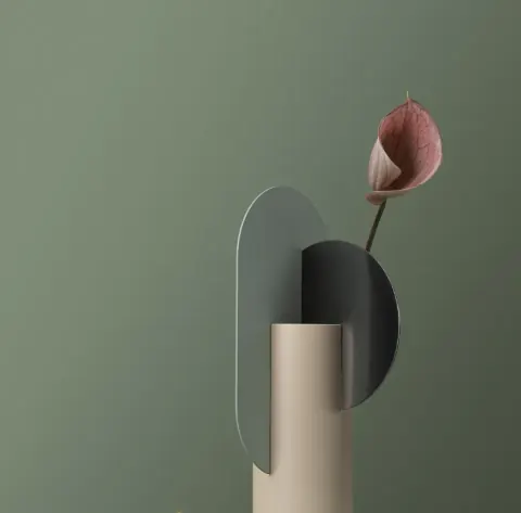 Pink calla lily in a sculptural vase against a sage green wall
